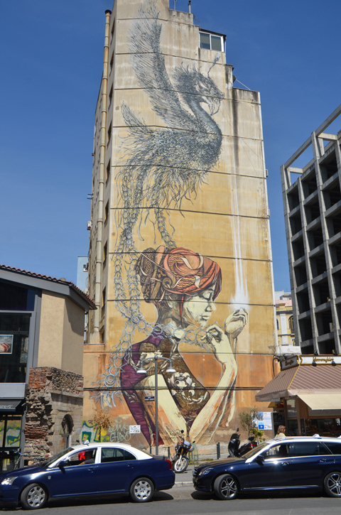 large mural on the side of a building, a woman in profile with her hair tied up, a feathery black bird above her 