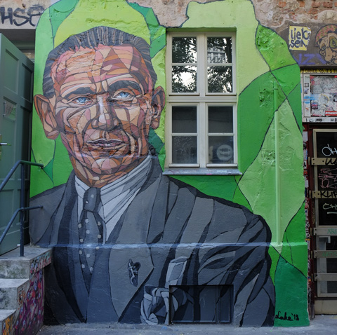 mural of man, large, in grey suit and shirt and tie, from chest up, short dark hair, blue eyes