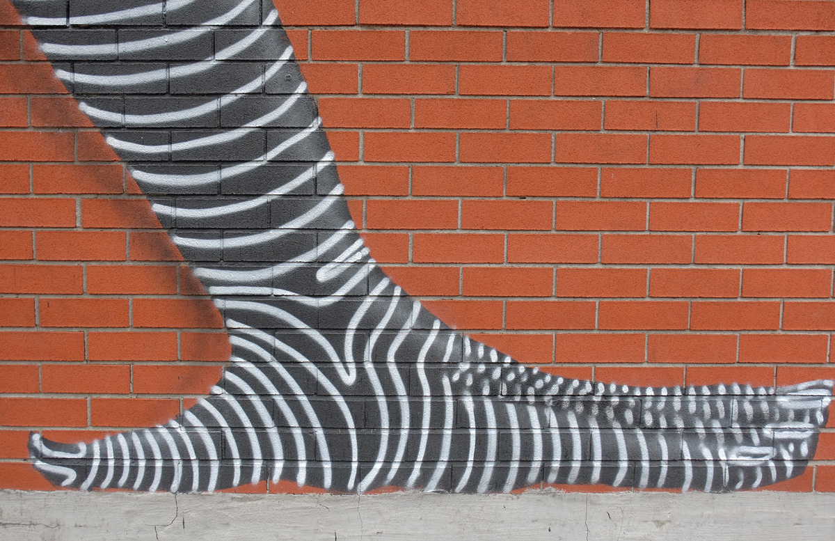 part of a larger mural, a black and white striped hand in on the ground, supporting two upside down figures 