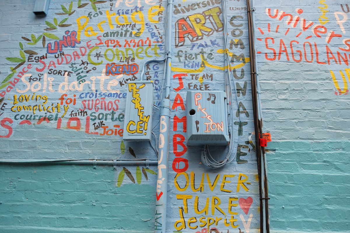 close up of part of street art mural in an alley, shape of a tree but filled in with words in different colours, words shuch as passion, communate, respect, fierte, English, French and Spanish words.