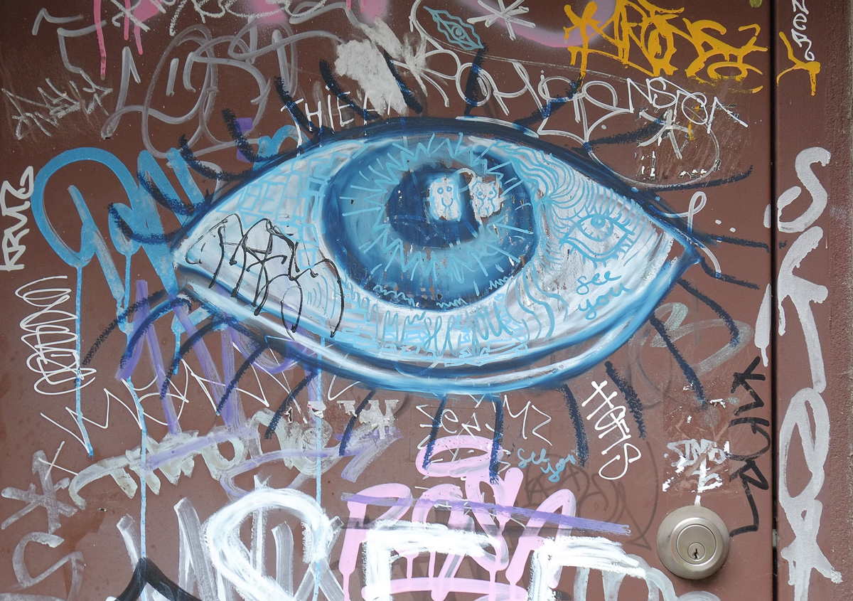 a bit blue eye painted on a brown door, with lots of graffiti around it. 