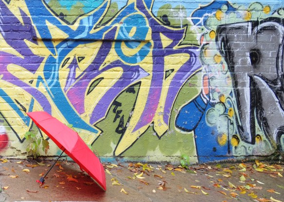 a red umbrella sits on the ground beside a mural 