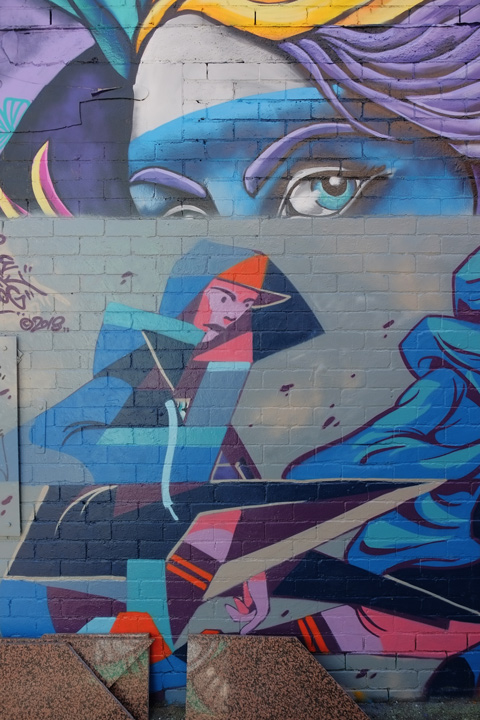 upper part is remains of a mural showing just a pair of woman's eyes, in blue, mural on the bottom of women working 