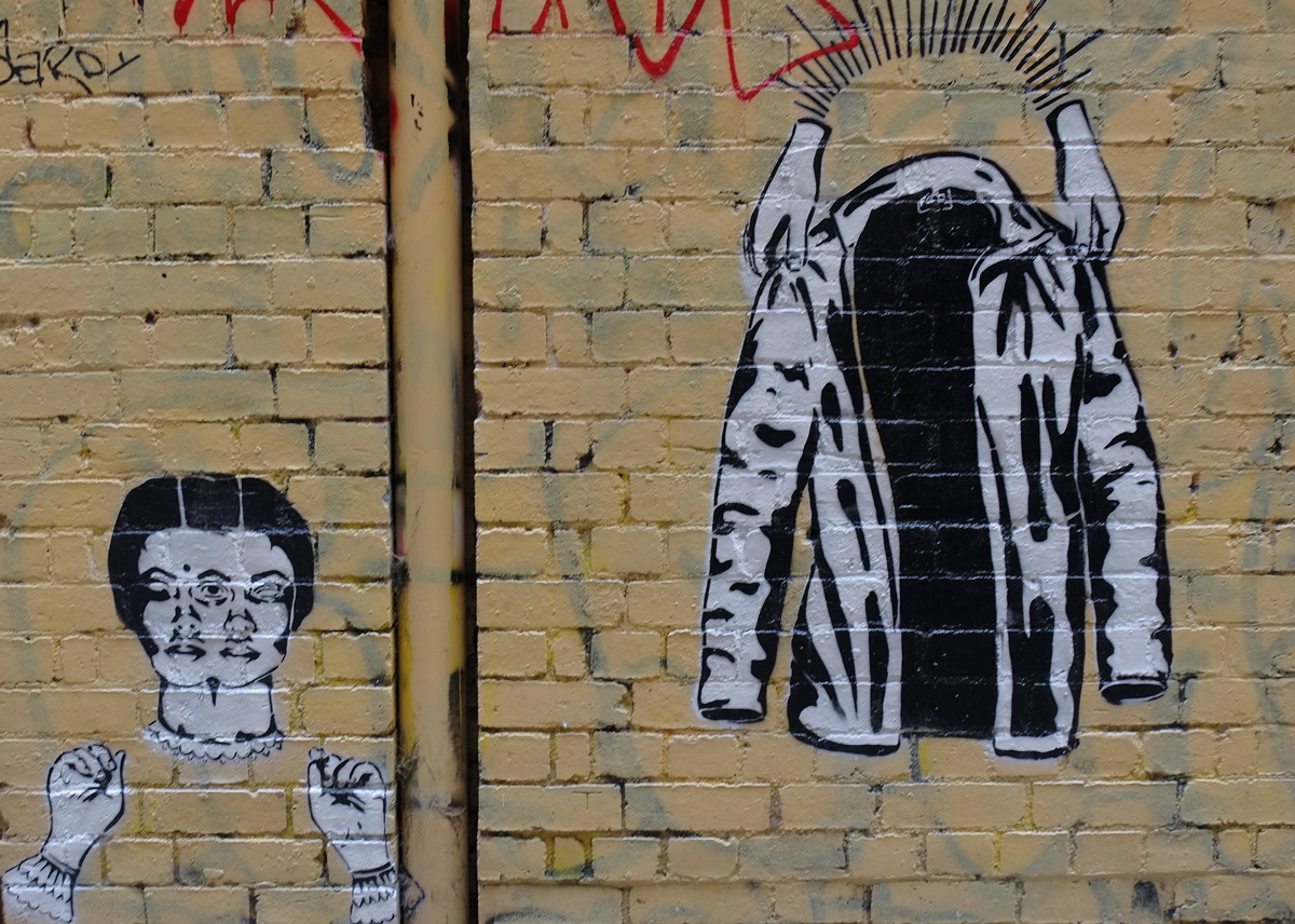 two black and white pasteups on a wall. on the right is a pair of white hands holding up an open jacket and on the left is a woman's head with two pairs of eyes, and a pair of hands below the head 