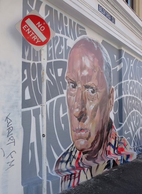 large painting of a man's head on the exterior wall, surrounded by grey words 