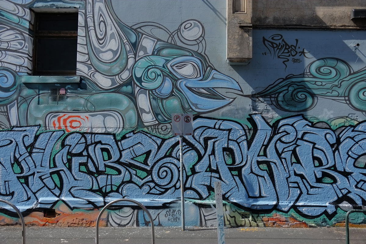 upper part is part of a mural by phibs in blues and greys of fish, drawn with lines and circles, the bottom part is a large blue tag. 