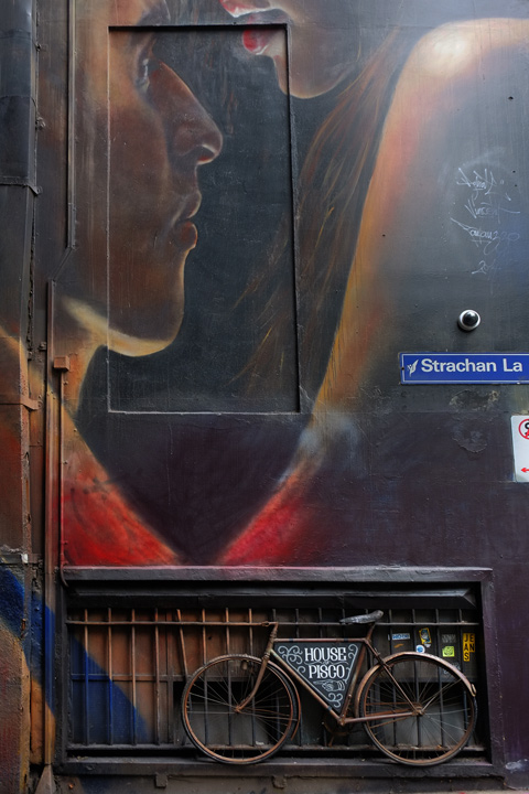 bike parked in front of a mural by adnate of a couple, street sign that says Strachan Lane 