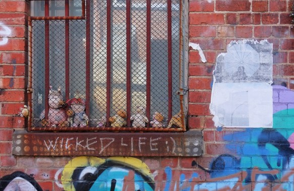 a row of stuffies behind a rusty metal grille in front of a window. 