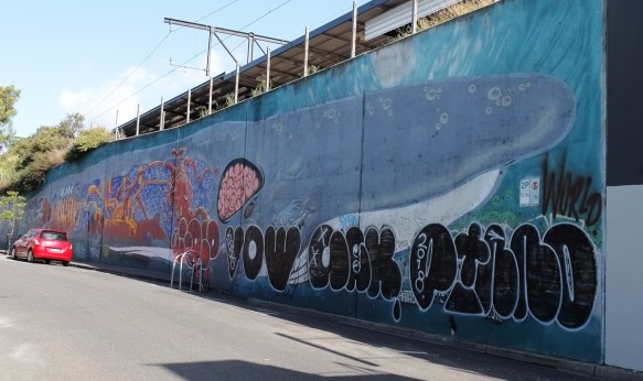 whale mural that is 40 metres long, on a wall, by train station, head of a whale, some black tags over it. 
