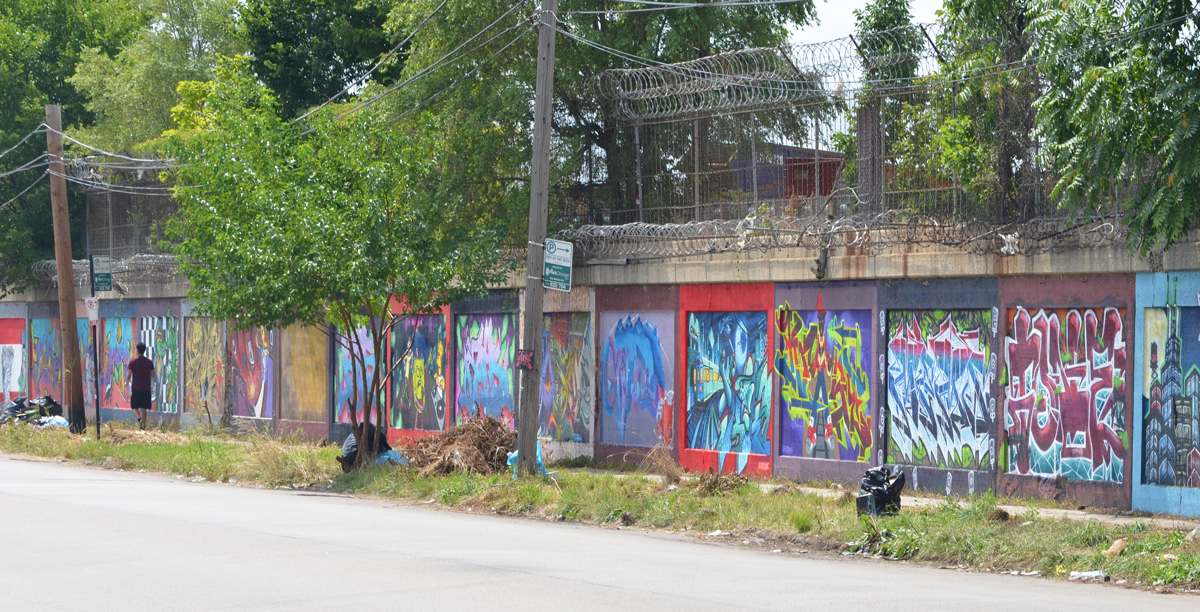a person walks past a wall covered with many murals beside a street, South Wood Street 