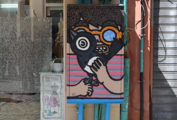 a painting on an electrical box on the street, of a boy with round orange glasses holding a large black bird 