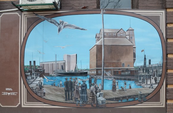 mural of an historic scene in Midland Ontario, people in fashion of the time, standing on dock looking at a boat in the water and a grain elevator 