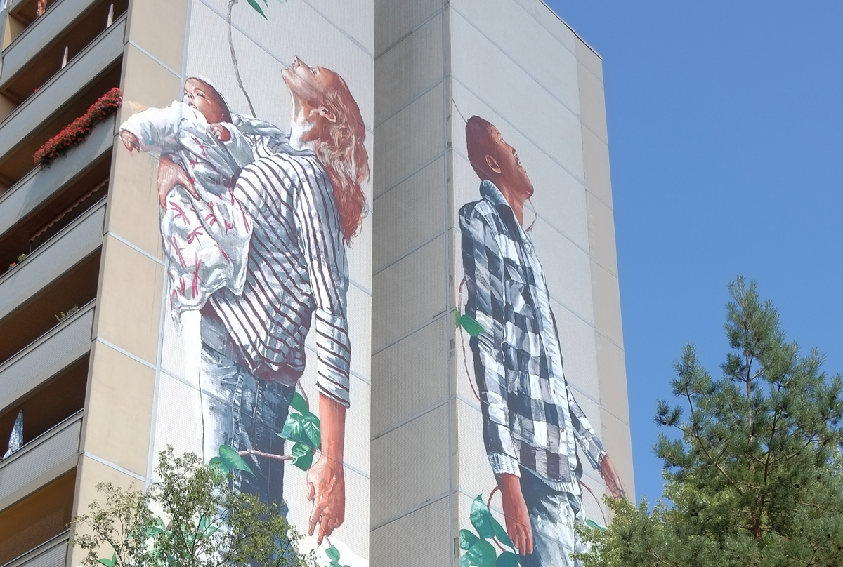 close up of upper part of mural, a mother and child on one side and a man, the father, on the other side,Urban Nation Tegel Art Park, large mural on side of 13 storey building, 