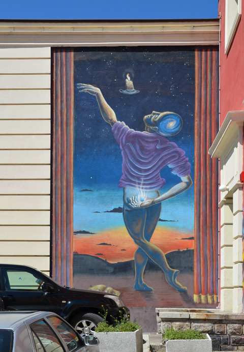 mural of a man from behind, one hand behind his back , the other hand in the air just released a candle, or is reaching for the candle 