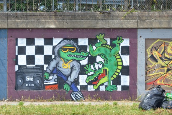mural on a concrete wall in Pilsen, two alligators or crocodiles, one in a hoodie and one standing on one front leg and smiling