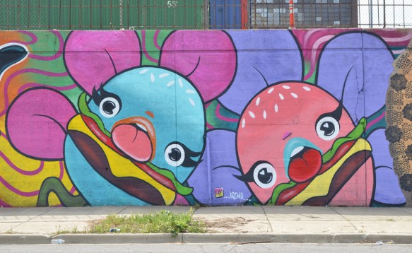 burger flowers mural by Branda Lopez in Chicago, two large flowers, one with pink petals and the other with purple petals, the centers are hamburgers with cheese, they also have faces and tongues that stick out