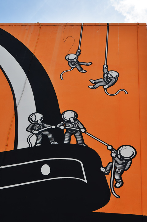 in a mural in Hollywood Florida, five small astronaut characters with ropes as they try to climb up