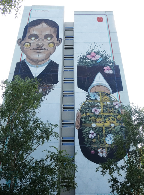 Pixel Pancho mural of two men, one with flower garden at the back of his head, Urban Nation Tegel Art Park, large mural on side of 13 storey building, 