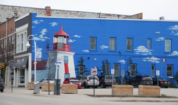 along the whole side of a building, painted bright sky blue with some puffy white clouds. A large painting of a red and white lighthouse 