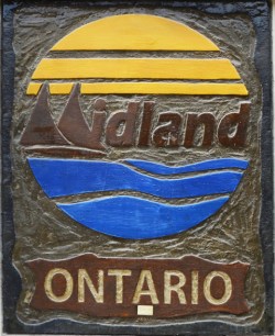 Midland ontario symbol in bronze with blue water, bronze pine trees and yellow sun