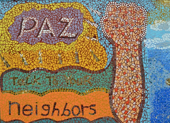 mosaic mural outside on a wall at 18th and Paulina in Pilsen area of Chicago, an arm raised with a fist along with the words paz, talk to your neighbors 