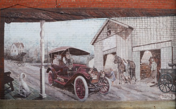 mural depicting a farm scene from a porch, with old fashioned car driving through. Barn with horse and child, also horse drawn wagon 
