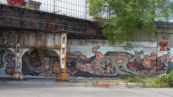 a mural that is partially under a railway bridge, metal supports for the bridge in the picture, 
