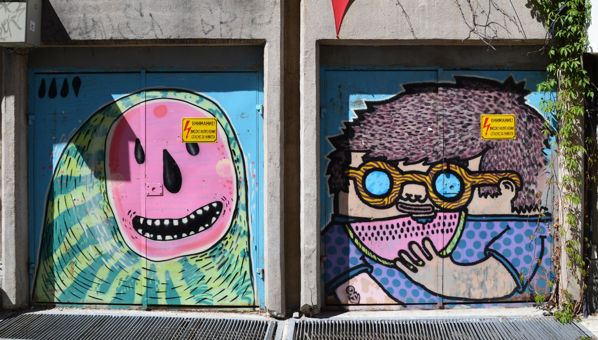 two murals side by side, one by mishka the mouse, and the other by aleksi varna. on the left is a watermelon cut open, seeds form a happy face, and the mural on the right is a person in round glasses eating a slice of watermelon 