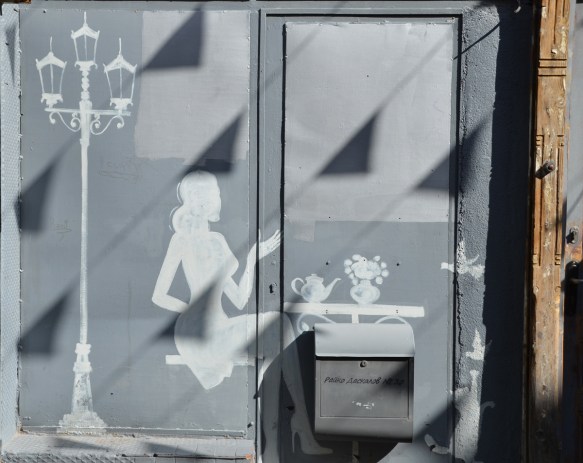All in white, like a silhouette, a tall lamp stand with three lamps at the top, a woman sitting beside a table with a tea pot and a vase on it. 