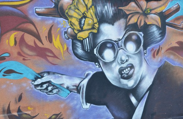 mural of a woman with large glasses and two flowers in her hair. she is holding something blue in one hand 