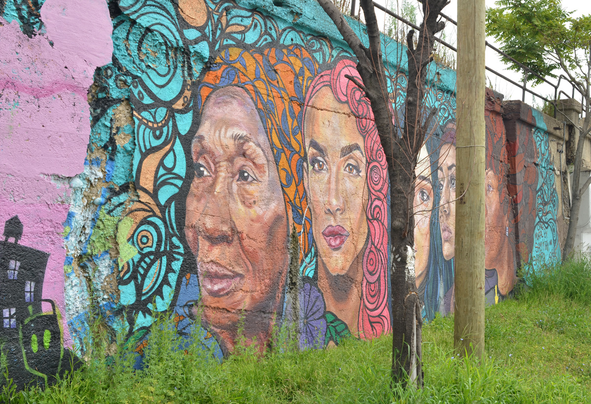 part of a mural by Sam Kirk and Sandra Antongiorgi of large women's heads, some trees in the way 