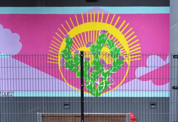 a mural behind a fence, pink, with yellow sun and green cactii 