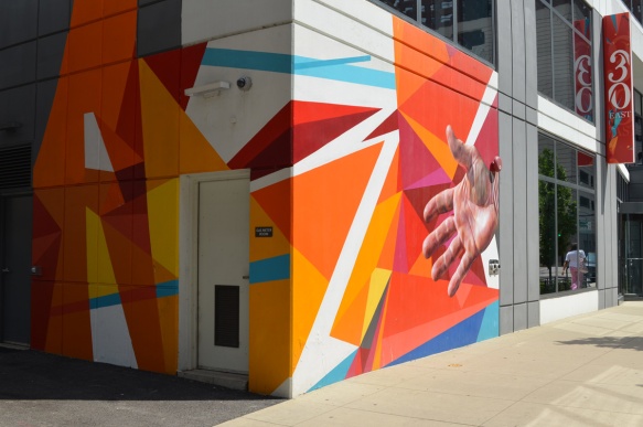 on the corner of a building, on both sides, a mural in bright oranges and reds, sharp edges, linear, with a realistic hand as well, 
