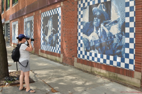 carol taking a picture of a row of murals of black musicians done in little squares on a brick wall in Chicago