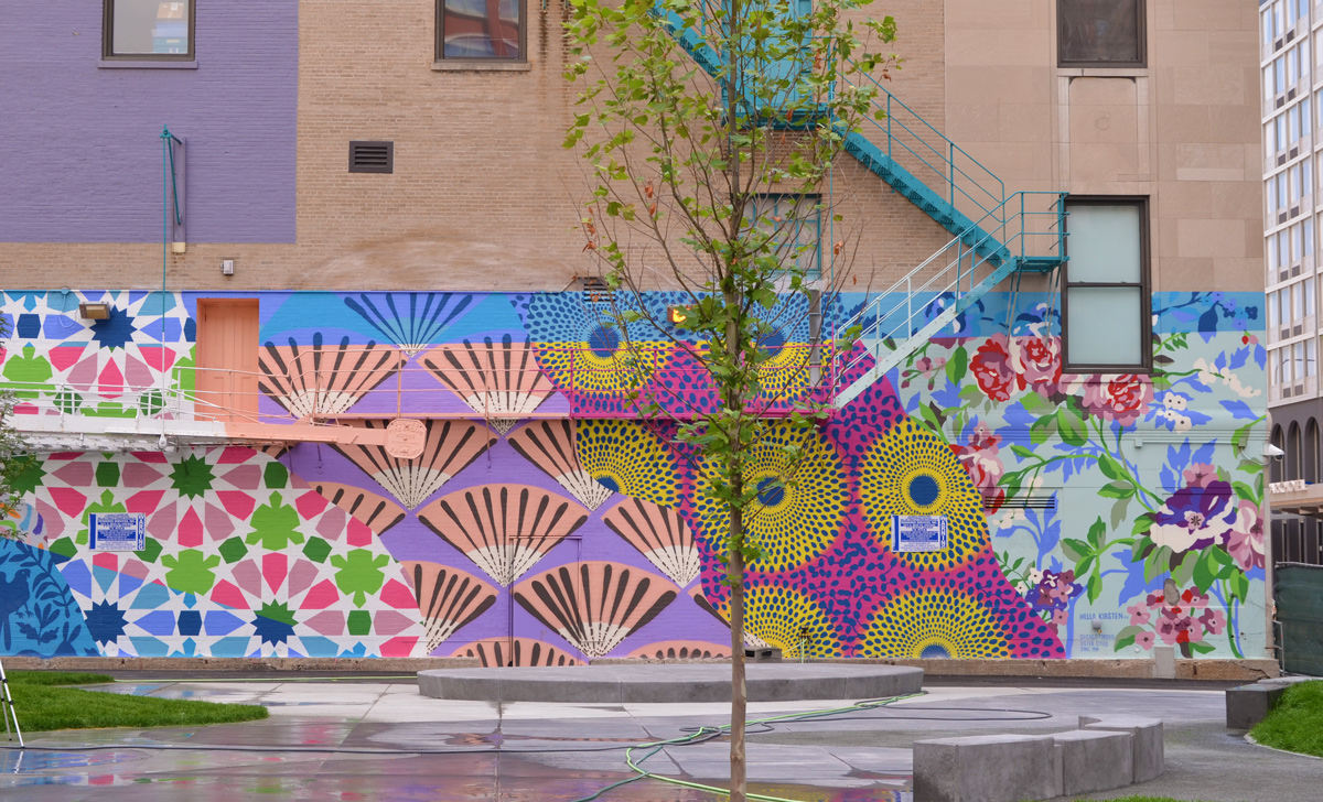 mural by Hello Kirsten on the side of a brick building with a blue exterior metal staircase
