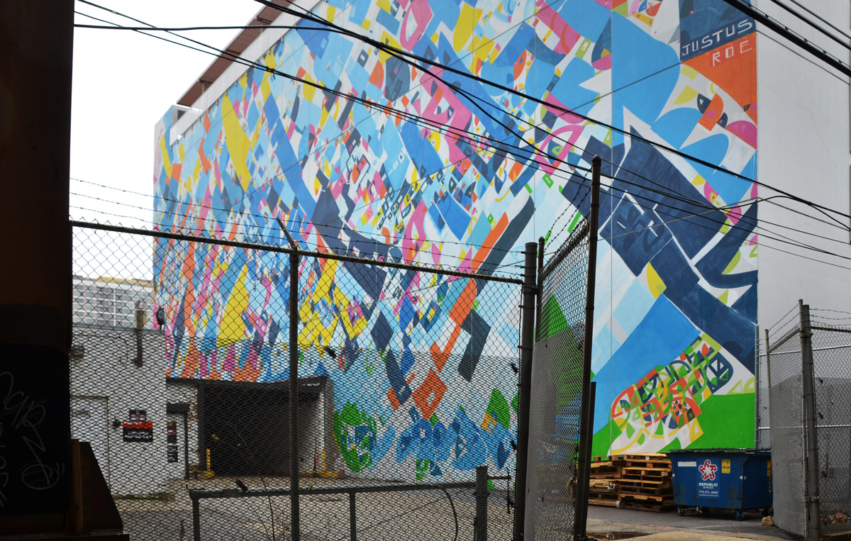 large abstract mural beside a parking lot, small area, also in a fenced in space 