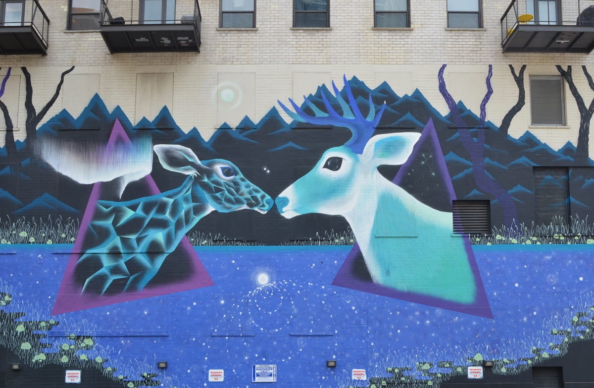 a mural by Marina Zumt of a doe and a buck, two deers, meeting nose to nose, painted in blues and purples 