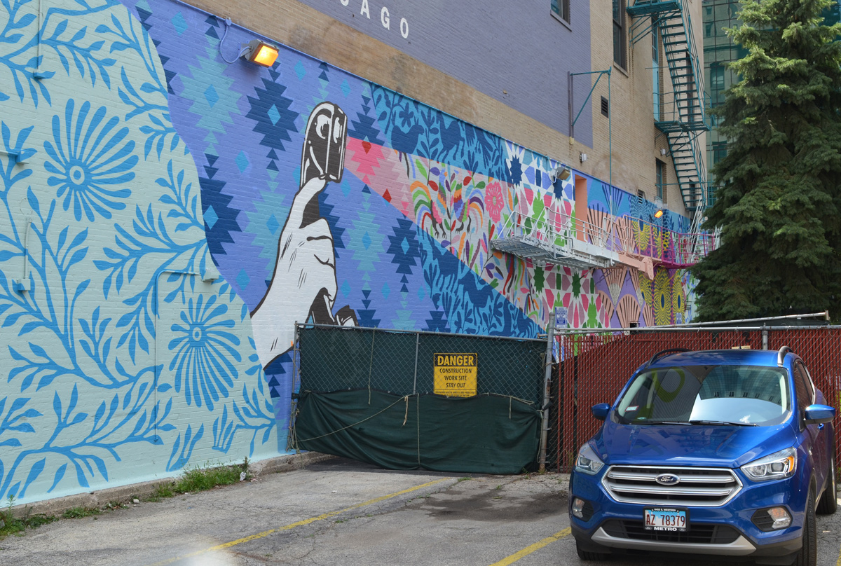 car parked beside a mural, large hand holding an old fashioned telephone receiver but using is as a flashlight 