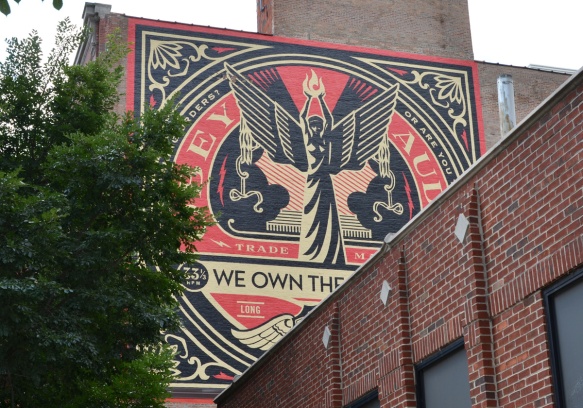 mural by obey in red, black, and gold, on upper storey of a brick building in Chicago