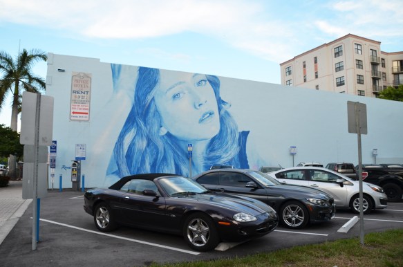 rone mural of a woman's head in blue tones - whole horizontal mural in parking lot with cars parked in front 