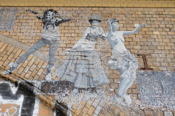 on a brick arch, a paste up in black white, life size picture of people dancing, three women, one in a long skirt, one topless
