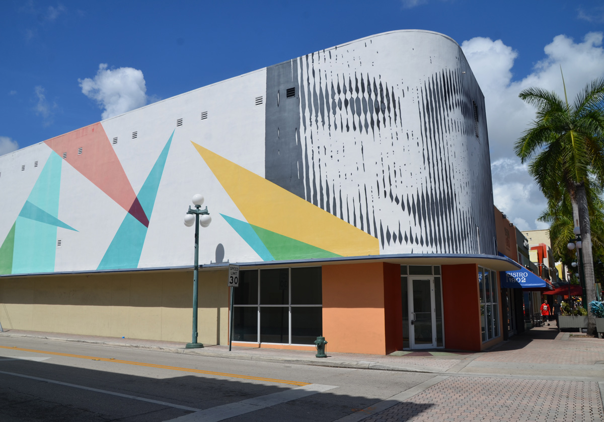 large face in grey tones made by vertical lines of differing darkness, over the entrance to a building, also shards of colour, triangles on white background