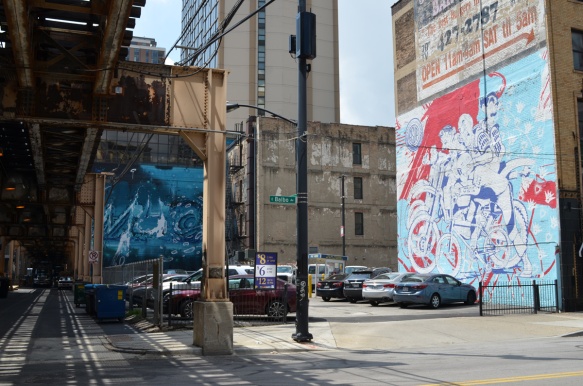 2 murals on Balbao street in Chicago, a blue one by a parking lot and one by asup on the side of a restaurant, 