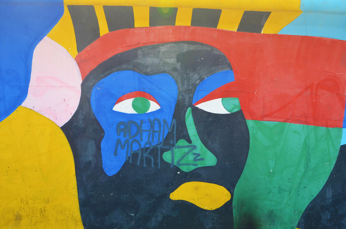stylized painting of a black face with yellow mouth, blue around one eye, red hair,