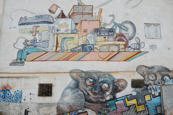 part of a larger mural wall, a painting by Kram of objecs on a flying carpet on the top, and smaller rodent like animals with beady eyes on the bottom 