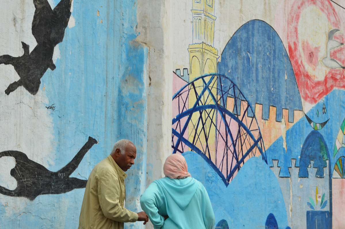 a man and a woman talking to each other as they stand in front of a wall covered in a series of murals