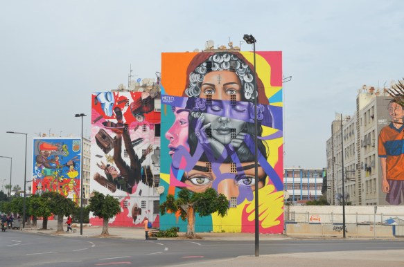 3 large murals at a Casablanca intersection, one in front is woman with many layered face