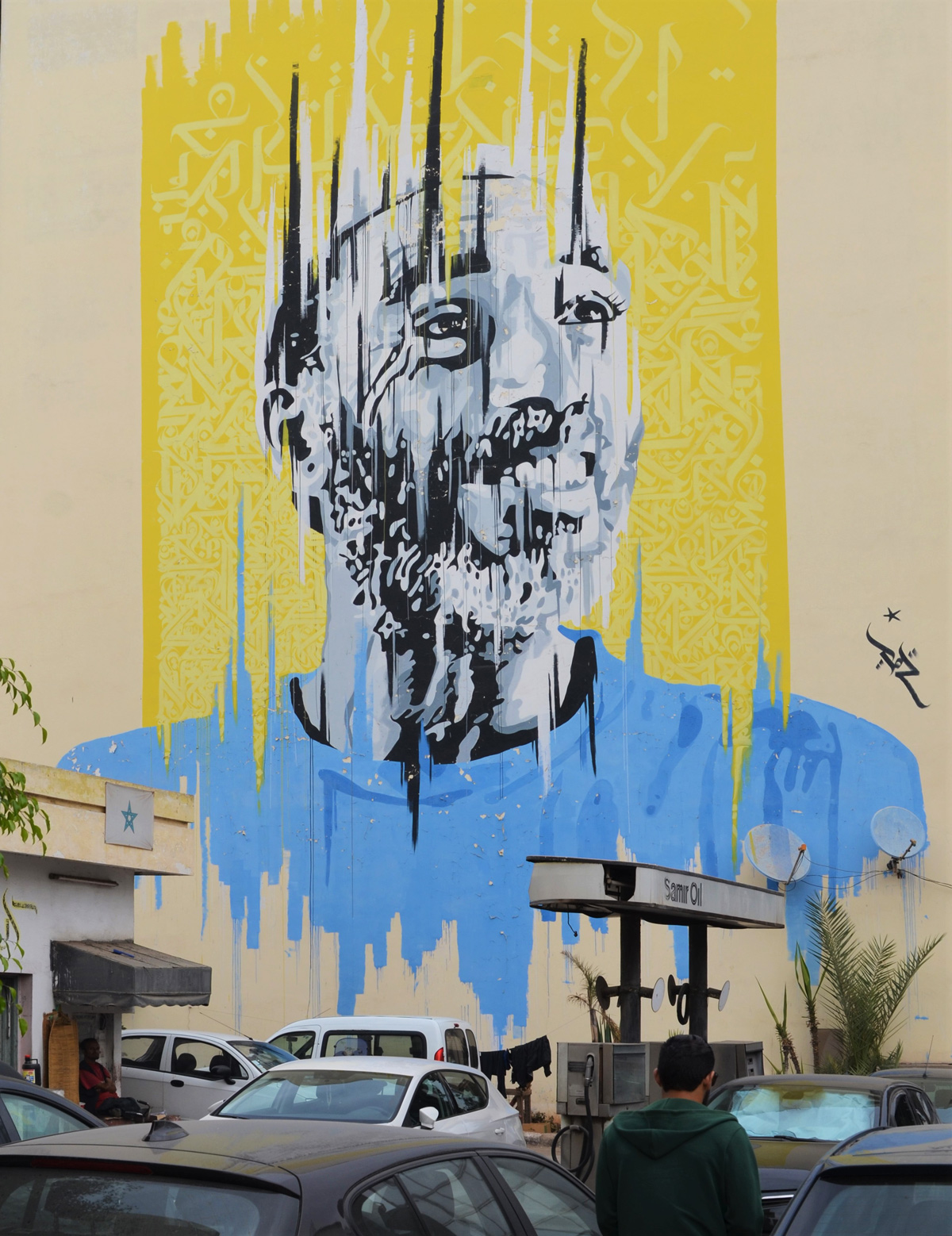 large mural painted by Yann Chatelin of a man in a blue T shirt, with yellow background, Casablanca gas station in the foreground
