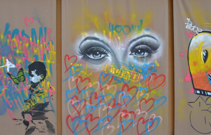 mural in sections, one section has two eyes in black and white surrounded by hearts in red and blue