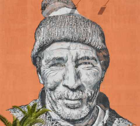 face of berber man in mural in Marrakech, part smile, wearing hat, mustache, wrinkled face 